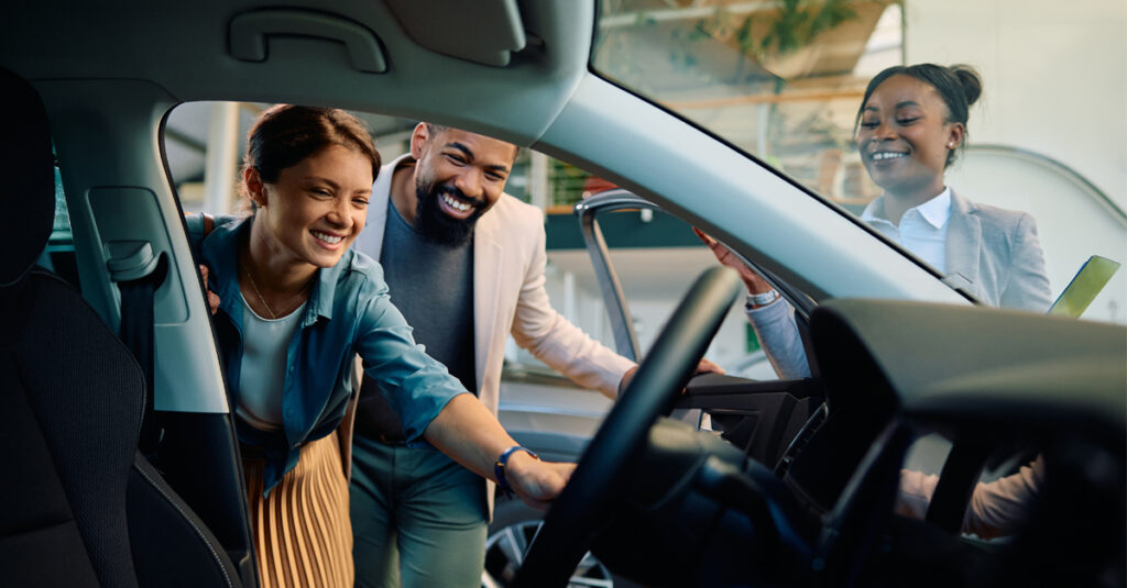 Smiling couple exploring new car interior with dealership sales consultant.